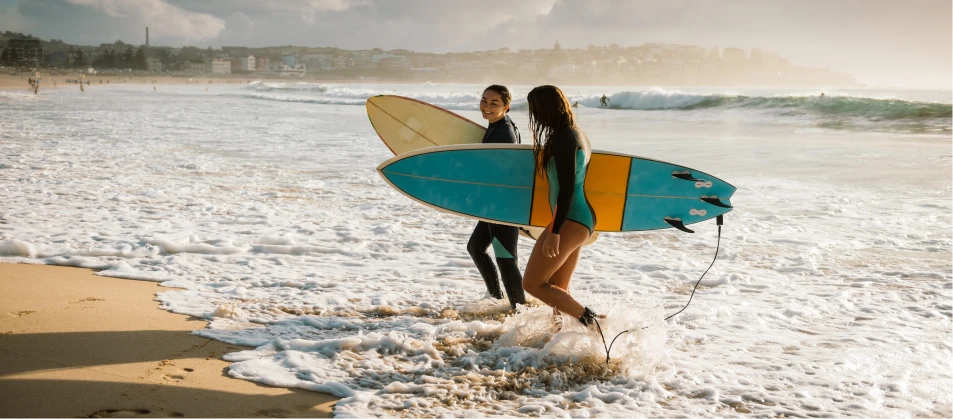 two women walking into the ocean with surfboards